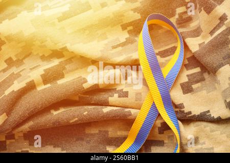 Gepixelter, digitaler Militärtarnstoff mit Band in blauen und gelben Farben. Attribute der ukrainischen patriotischen Soldatenuniform. Gepixelt digital Stockfoto