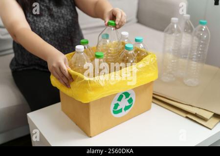 Recyceln Sie die umweltfreundliche Zero Concept Frau, die leere Plastikflasche mit gelben Mülltüten zu Hause in den Recyclingbehälter wirft Stockfoto