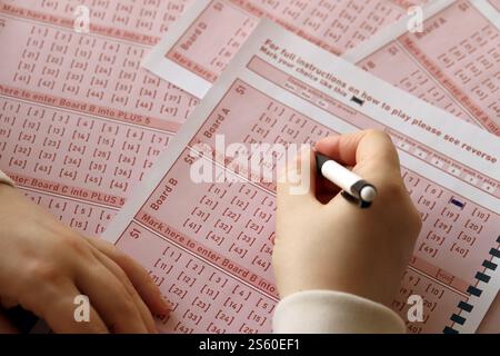 Ein Lotterielos ausfüllen. Eine junge Frau spielt im Lotto und träumt davon, den Jackpot zu gewinnen. Weibliche Handzeichen auf rotem Lotterielos Stockfoto