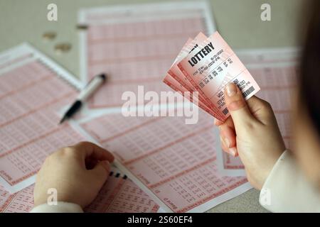 Ausfüllen eines Lottotickets. Eine junge Frau hält das Lottoticket mit vollständiger Zahlenreihe auf dem Hintergrund der Lotterie. Glücksspiel Stockfoto
