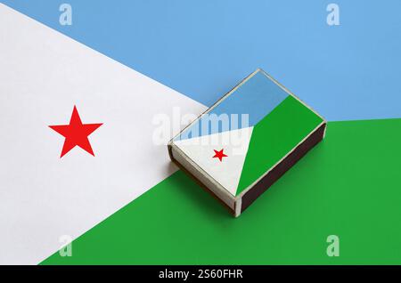 Die Flagge Dschibuti ist auf einer Streichholzschachtel abgebildet, die auf einer großen Flagge liegt. Die Flagge Dschibuti ist auf einer Streichholzschachtel abgebildet, die auf einer großen Flagge liegt Stockfoto