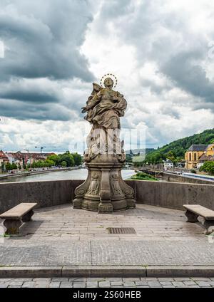 Eine detailgetreue Steinstatue auf einer historischen Brücke über einen ruhigen Fluss, umgeben von malerischer Architektur und üppigem Grün unter einer dramatischen Wolke Stockfoto