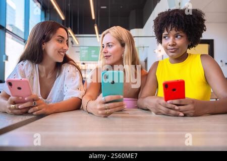 Drei Frauen, die sich mit Smartphones in einem modernen Café unterhalten Stockfoto