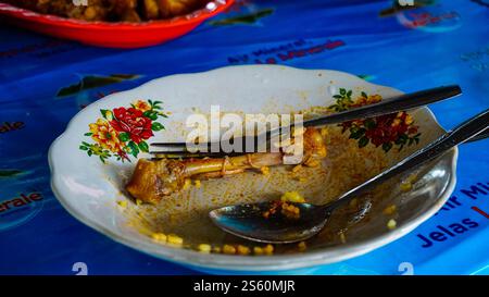 Ein leerer Teller mit Hühnerknochen und Resten auf einer blauen Tischdecke. Stockfoto