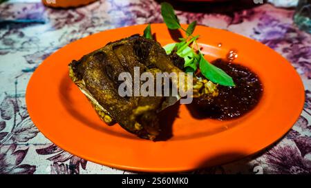 Ein frittiertes Stück Fleisch, serviert auf einer Orangenplatte mit einer Sauce und garniert mit frischen Kräutern. Stockfoto