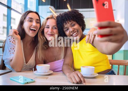 Drei glückliche Freunde machen ein Selfie, während sie Kaffee in einem modernen Café genießen Stockfoto