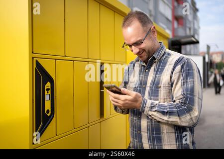 Happy man sammelt das Paket aus einem hellgelben Schließfach in urbaner Umgebung Stockfoto