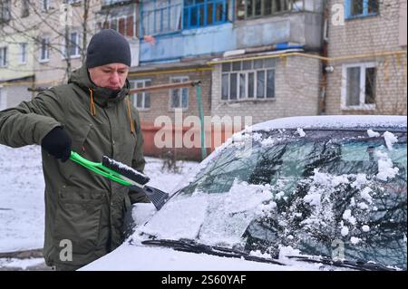 Ein Mann entfernt Schnee von einem Auto. Eis abkratzen Stockfoto