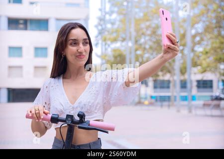 Eine junge Frau, die ein Selfie macht, während sie einen Elektroroller hält Stockfoto