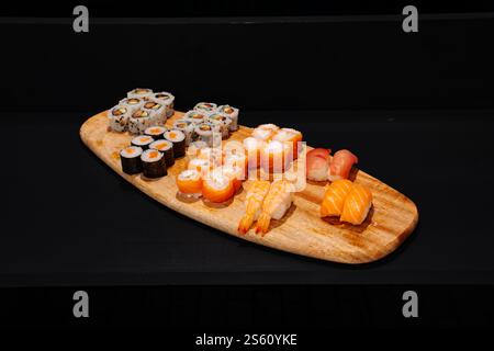 Kreative, minimalistische Präsentation verschiedener Sushi-Brötchen auf einer Holzplatte vor dunklem Hintergrund, die lebendige Farben und exquisite japanische Cul betont Stockfoto