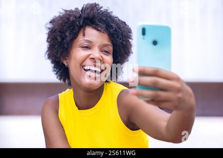 Aufgeregt afroamerikanische junge Frau, die draußen ein Selfie mit einem Smartphone macht Stockfoto