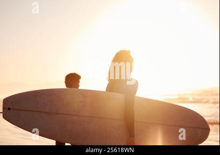 Silhouette, Sonnenaufgang oder Sonnenuntergang mit Surferpaar am Strand, Meer oder Meer am Morgen als Training oder Workout. Surfbrett, Wassersport und gesund Stockfoto