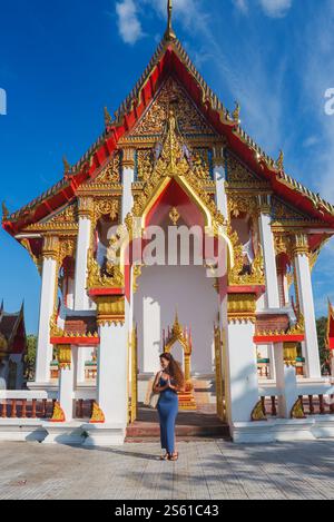 Frau in Blau steht vor dem kunstvollen thailändischen buddhistischen Tempel im Sonnenlicht Stockfoto