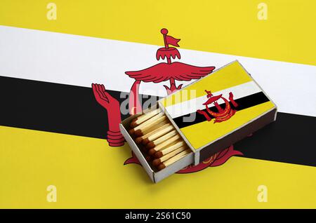 Brunei Darussalam Flagge wird in einem offenen Streichholzkasten gezeigt, der mit Streichhölzern gefüllt ist und auf einer großen Flagge liegt. Die Flagge von Brunei Darussalam wird in einem angezeigt Stockfoto