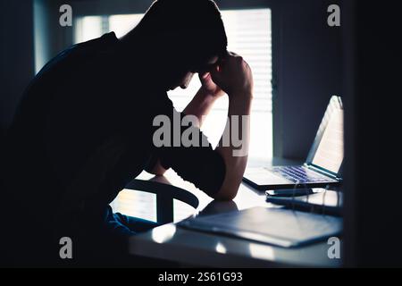 Stress am Arbeitsplatz. Müder Mann mit Angst. Trauriger Büroangestellter mit Laptop. Frustrierter Student oder Student. Dunkle Silhouette eines ängstlichen Menschen. Stockfoto