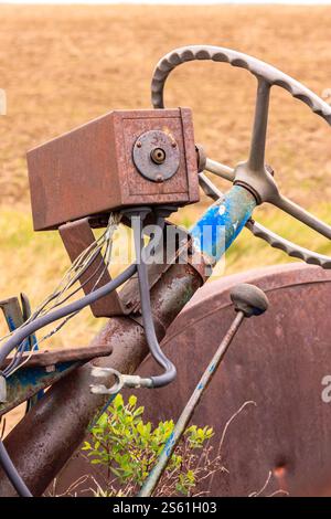 Ein rostiger alter Traktor mit blauem Lenkrad. Das Lenkrad fehlt, und der Traktor befindet sich auf dem Feld Stockfoto