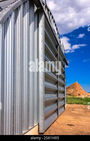 Ein großes Metallgebäude mit einer Pyramide im Hintergrund. Das Gebäude ist von einem Feld umgeben und der Himmel ist klar Stockfoto