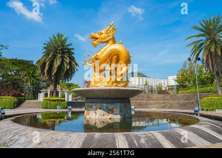 Goldene Drachenstatue auf einem runden Brunnen, umgeben von Gärten, Palmen und modernen Gebäuden unter einem hellblauen Himmel in Phuket, Thailand. Stockfoto