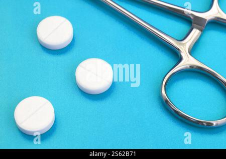 Mehrere weiße Tabletten und eine medizinische Schelle liegen auf einem hellblauen Hintergrund Oberfläche. Hintergrundbild über medizinische und pharmazeutische Themen Stockfoto