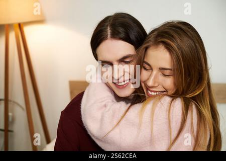 Zwei junge Erwachsene genießen einen fröhlichen Moment zusammen, in die Arme gewickelt und hell lächelnd. Stockfoto