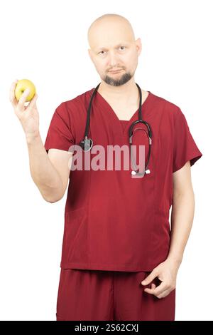 Ein glatzköpfiger Arzt trägt rote medizinische Peelings und ein Stethoskop um den Hals, hält einen grünen Apfel. Stockfoto