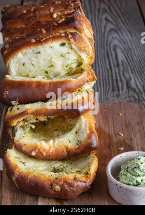 Hausgemachtes frisches Pull-Apart-Brot mit Kräutern (Petersilie, Thymian, Rosmarin, Dill), Knoblauch, Käse und scharfe Butter auf einem Holzbrett. Stockfoto