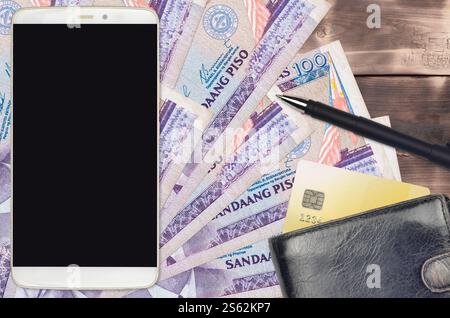 100 philippinische Piso-Rechnungen und Smartphone mit Geldbörse und Kreditkarte. E-Zahlungen oder E-Commerce-Konzept. Online-Shopping und Business mit tragbaren Geräten Stockfoto