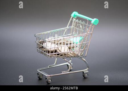 Ein metallischer Mini-Einkaufswagen, Trolley, gefüllt mit Stapeln von Münzen, Sterling, symbolisiert Sparen, Investitionen und Geschäftstransaktionen Stockfoto