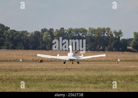 Ein kleines weißes Propellerflugzeug, das auf einer grasbewachsenen Landebahn unter freiem Himmel ruht Stockfoto