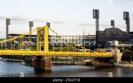 Pittsburgh, Pennsylvania, USA - 8. August 2023: Ein beeindruckender Blick auf eine gelbe Brücke über dem Wasser, mit einem Stadion und einer Skyline der Stadt im Hintergrund bei Sonne Stockfoto