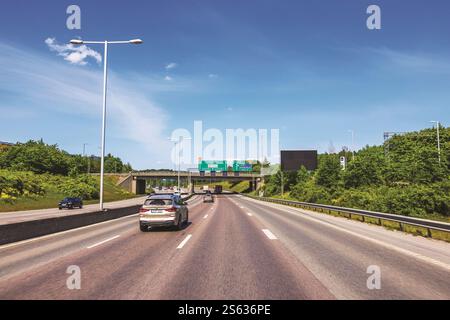 Autos fahren auf der Autobahn unter klarem blauem Himmel mit Straßenschildern und Brücke im Hintergrund an sonnigen Tagen. Stockfoto