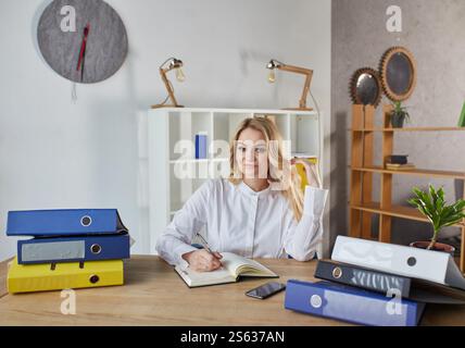 Porträt einer glücklichen Geschäftsfrau, die sich Notizen macht, während sie im Büro am Tisch sitzt. Stockfoto