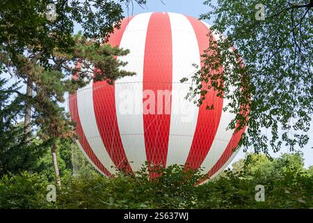 Rot-weißer Heißluftballon auf dem Boden hinter den Bäumen Stockfoto