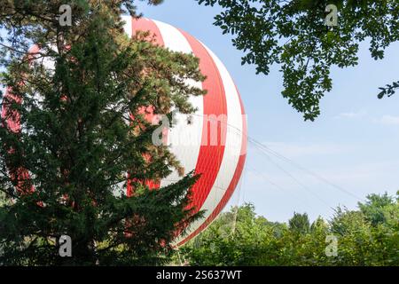 Rot-weißer Heißluftballon auf dem Boden hinter den Bäumen Stockfoto