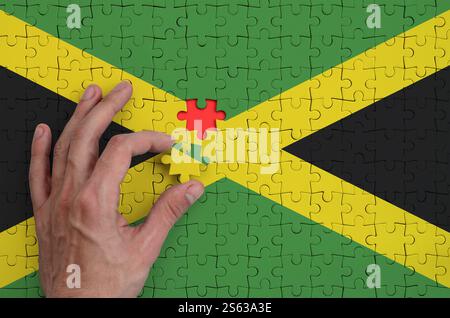 Die Jamaika-Flagge ist auf einem Puzzle abgebildet, das die mannische Hand zum Falten vervollständigt. Die Jamaika-Flagge ist auf einem Puzzle abgebildet, zu dem die bemannte Hand vervollständigt Stockfoto