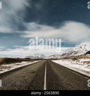 Sternenklare Nacht über einer schneegesäumten Straße, die zu zerklüfteten Bergen in Hornafjörður, Süd-Island, führt. Stockfoto
