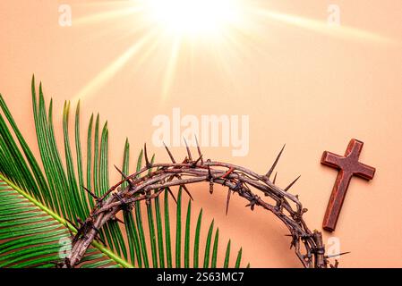Dornenkrone, hölzernes chriatisches Kreuz und Palmblätter auf rosa orangefarbenem Hintergrund mit abstraktem Sonnenlicht. Karwoche, Fastenzeit, Palmsonntag, Karfreitag, E Stockfoto