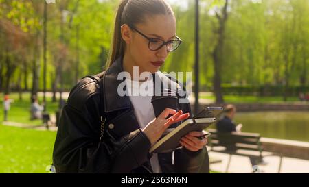 Kaukasische Frau Geschäftsfrau mit Handy Smartphone Telefon Technologie Arbeit online Trinken Take Away Kaffee Walking Park weibliche Arbeitgeber Stockfoto