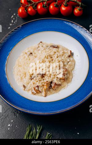 Cremiges Stachelpilz-Risotto auf blauem Teller mit Parmesan-Beilage Stockfoto