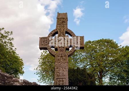 Ein großes Steinkreuz mit einem Kreis in der Mitte. Der Himmel ist blau und es gibt Bäume im Hintergrund Stockfoto