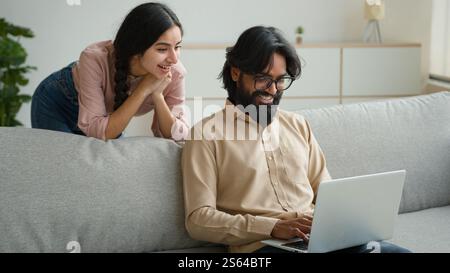 Arabian Indianerpaar auf Couch Sofa benutzen Computer Laptop Shopping online Internet Shop glückliche multirassische Frau Ehemann lächelnd schöne Kunden Frau Stockfoto