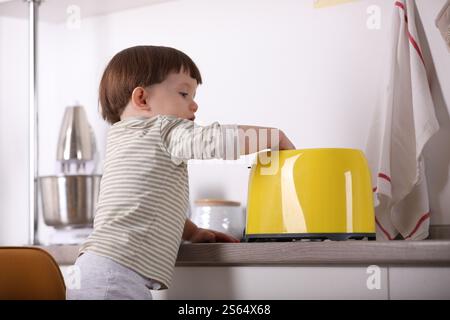 Kleiner Junge, der mit Toaster in der Küche spielt. Gefährliche Situation Stockfoto