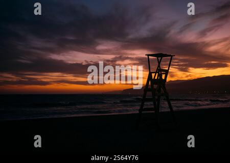 Der Rettungsschwimmer-Turm ist vor einem lebhaften Sonnenuntergang an einem abgeschiedenen Strand umgeben Stockfoto