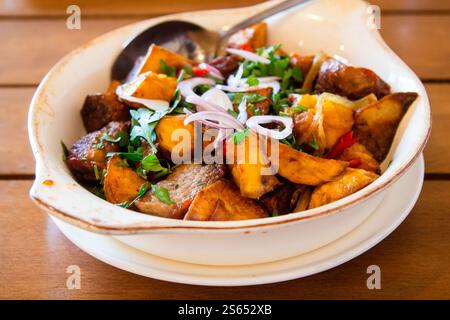 Reisen Sie nach Georgien - Portion Ojakhuri (georgisches Gericht, gebratenes Fleisch mit Kartoffeln) in einer Schüssel auf Holztisch im lokalen Café in Batumi City Stockfoto