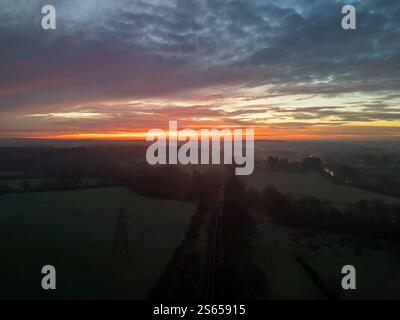 Aus der Vogelperspektive des farbenfrohen Sonnenaufgangs, der nebelige Felder und die Eisenbahn in der Nähe von Plymouth, Devon, England beleuchtet und eine atemberaubende Winterlandschaft schafft Stockfoto