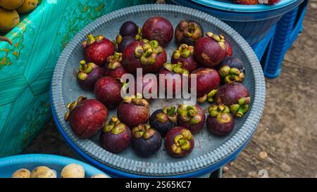 Ein Teller gefüllt mit frischen Mangostanen auf einem Marktstand, umgeben von anderen Früchten. Stockfoto