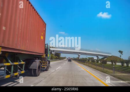 Ein Anhänger-LKW mit Container fährt auf der linken Spur auf einer mautpflichtigen Straße in Indonesien. Blickwinkel aus dem Inneren eines Autos, das einen Lkw überholt i Stockfoto