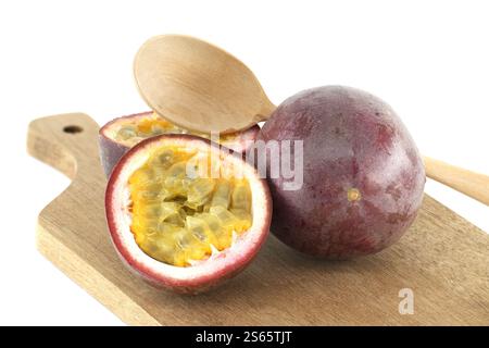 Reife Passionsfrüchte, Passiflora edulis, mit Holzlöffel, der auf Holzbrett liegt und das saftige gelbe Fruchtfleisch und die Samen zeigt, fertig zum Verzehr oder Stockfoto