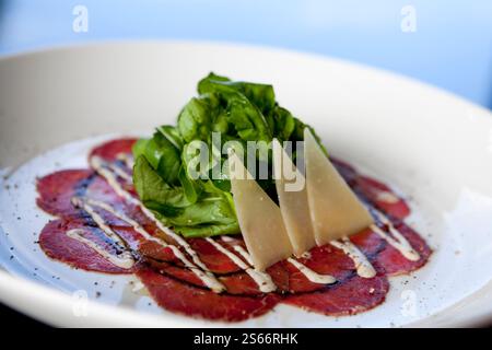 In Scheiben geschnittener roher Rindercarpaccio Rucola-Salat mit Parmesan. Carpaccio ist dünn geschnittenes oder zerstampftes Fleisch und wurde in Venedig, Italien, hergestellt. Stockfoto