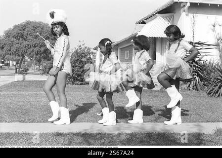 Üben für die große Parade 1968. Vier Mädchen ziehen vor dem Fotografen in Uniform. Eine Übung, die sie auf der Einfahrt eines Hauses in Los Angeles vor der großen Parade machen. Die vier Mädchen tragen festliche Kleidung und weiße Stiefel. Der älteste geht zuerst als Trommelmajor, der die zeremonielle Keule trägt. USA 1968. Roland Palm Ref. 15-5-20 Stockfoto